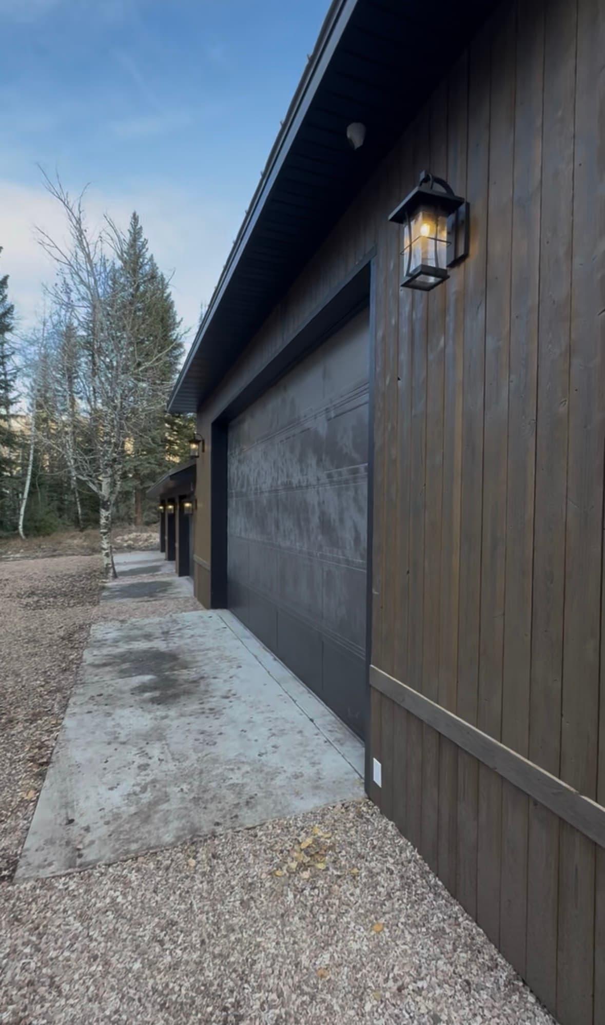 Modern garage with dark wood siding, a black door, and warm outdoor lantern lighting.