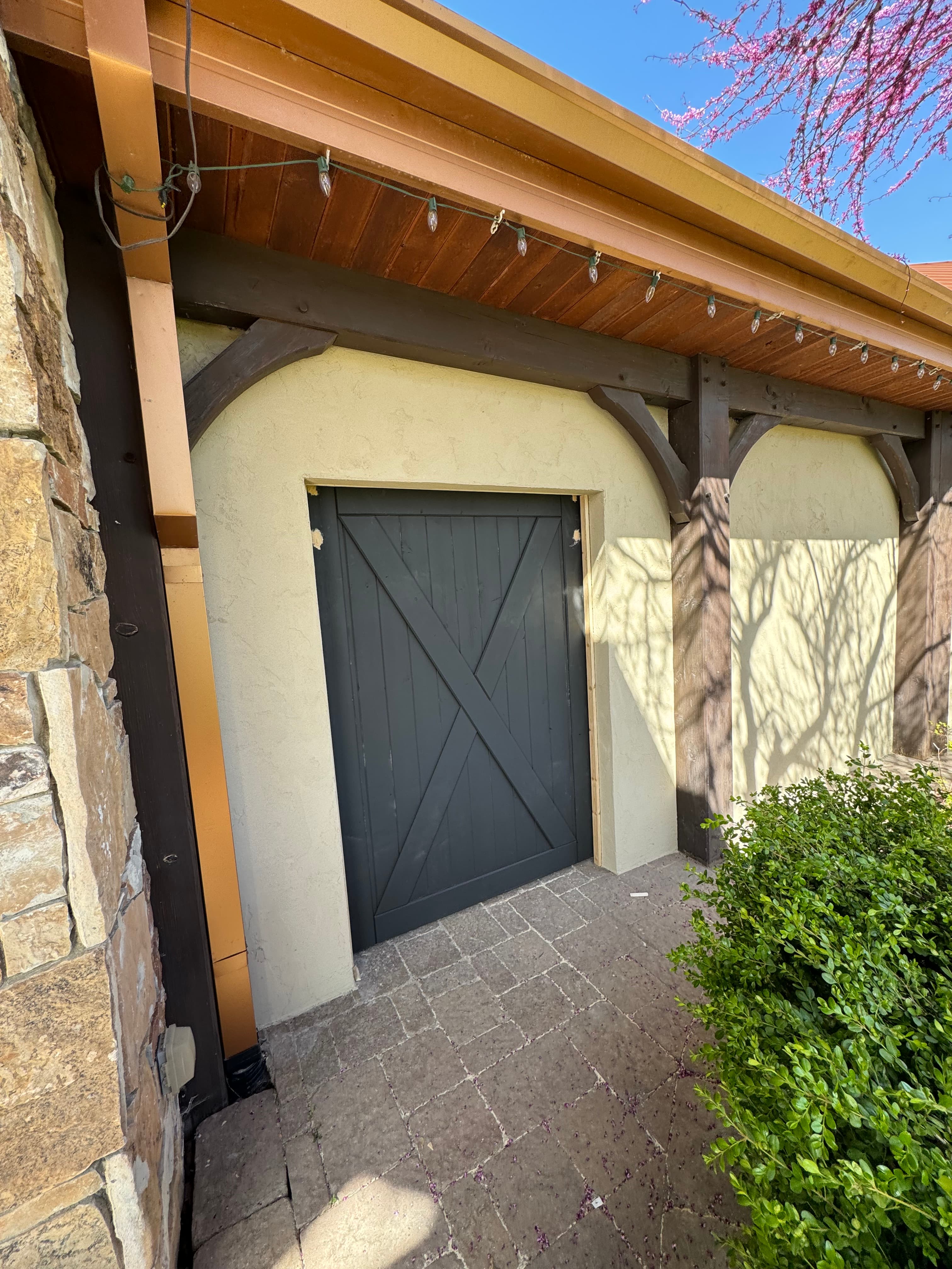 Black barn-style door with X-brace on cream stucco wall with dark wood timber framing.